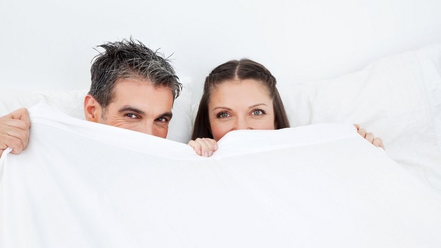 Nettes Paar sitzt entspannt unter einer dicken Winterbettdecke