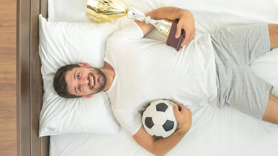 Junger Mann feiert Fussball EM im bequemen Bett